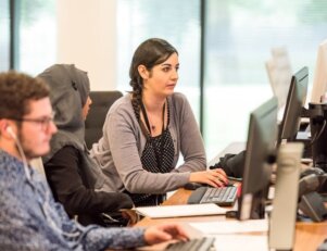 Três pessoas sentadas em frete a computadores em um escritório