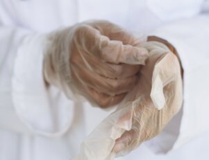 Profissional de um dos níveis de atuação na Enfermagem colocando luvas.