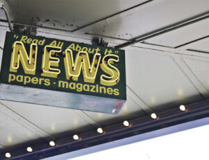 letreiro no alto pendurado no teto com a frase read all about it news paper magazines em amarelo com fundo verde imagem para tema de ética jornalística