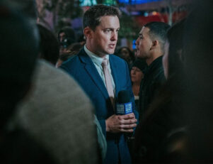 Homem de terno com um microfone no meio de várias pessoas