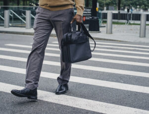 Homem vestido em roupas sociais, segurando uma maleta, enquanto atravessa uma faixa de pedestres