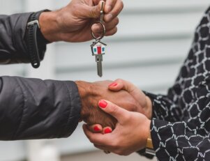 Pessoa entregando as chaves de um imóvel, enquanto aperta as mãos de outra